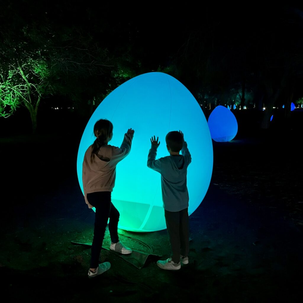 Silouette of kids in front of giant glowing egg art thing.