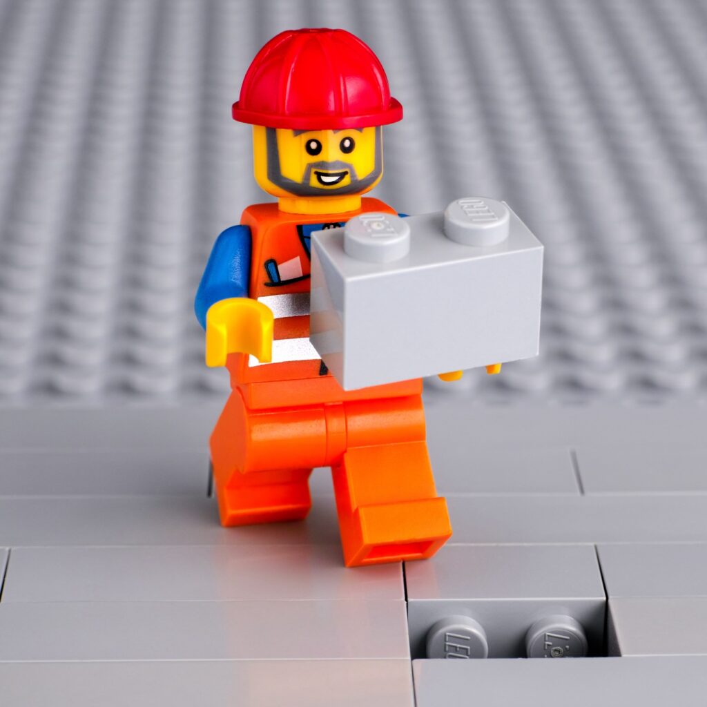 Lego man placing the last brick to finish the floor.